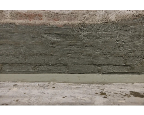 Close-up van een gepleisterde bakstenen muur en een cementvloer.