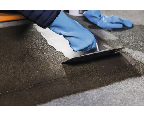 Persoon draagt handschoenen en dicht een vloer af met een plamuurmes