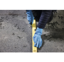 Persoon met werkhandschoenen, waterpas en stanleymes die een materiaal snijdt