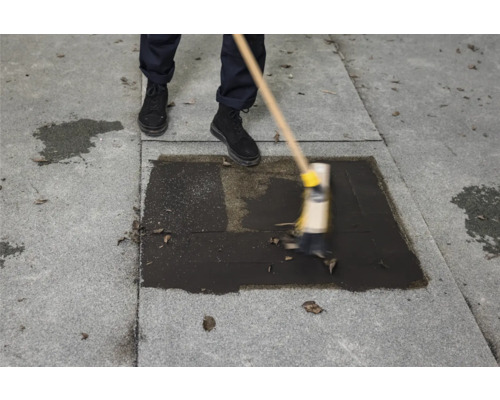 Een persoon maakt een dakgoot schoon met een borstel op een dak.