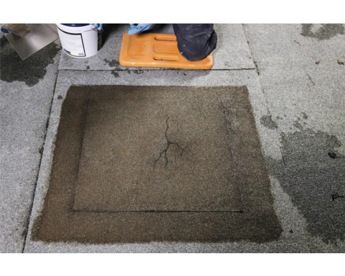 Reparatie van een beschadigde bitumineuze dakbaan met vloeibare bitumencoating.