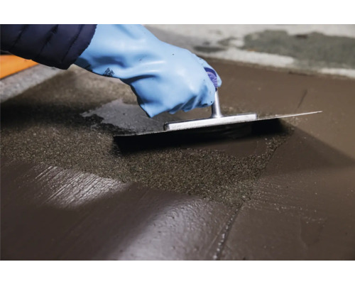 Persoon egaliseert vloermassa met een spaan