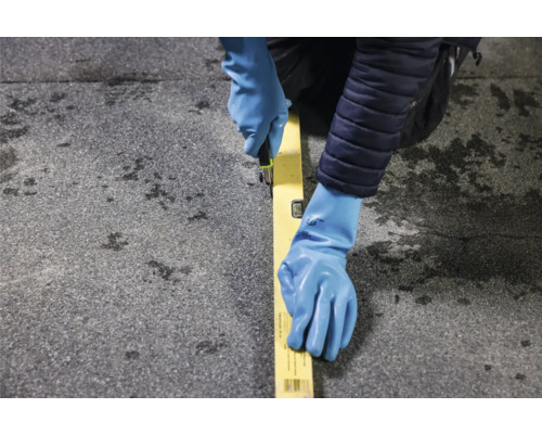 Een persoon met handschoenen die met een mes langs een liniaal op een oppervlak snijdt