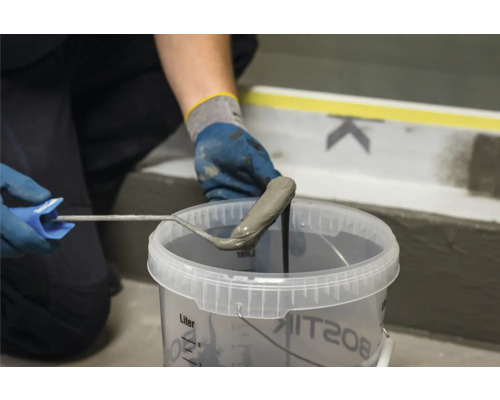 Vakman doopt verfroller in een emmer met afdichtingsslib voor bouwwerkzaamheden