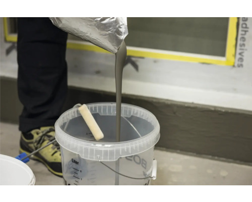 Gietvloermassa wordt in een transparante emmer met verfroller gegoten