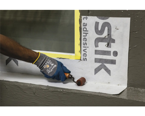 Een persoon gebruikt een rol om afdichtingsbanen op een raam aan te brengen.