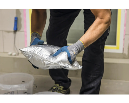 Iemand houdt een zilverkleurige zak met materiaal voor bouwwerkzaamheden vast.