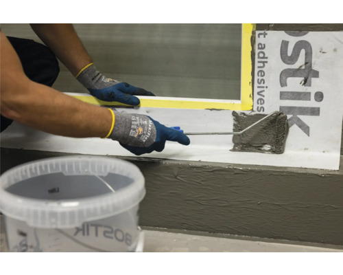 Persoon brengt afdichtmiddel aan met een rol, met Bostik Logo op de achtergrond