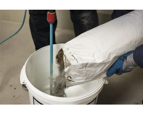 Iemand giet materiaal uit een zak in een emmer met een roerwerk.