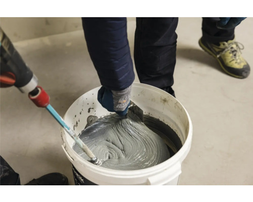 Ambachtsman mengt tegellijm in emmer met roerwerk en plamuurmes