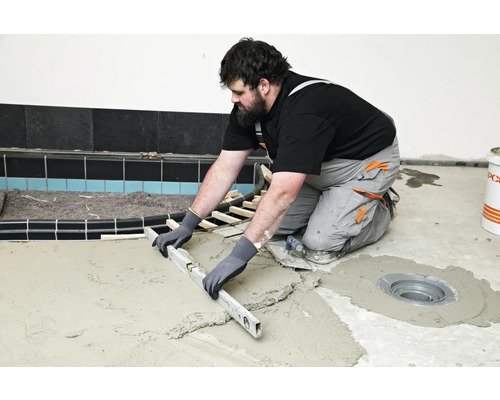 Ambachtsman egaliseert dekvloer met een waterpas in de badkamer.