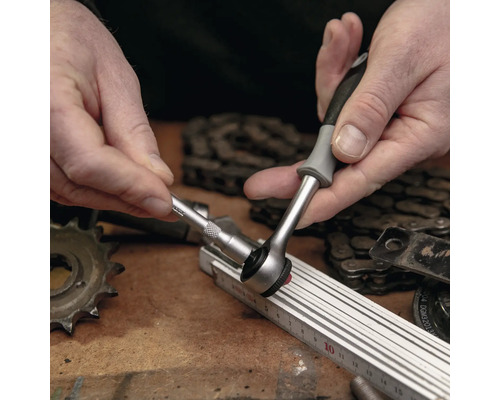 Een persoon gebruikt een ratel met dopsleutel op een werkbank.