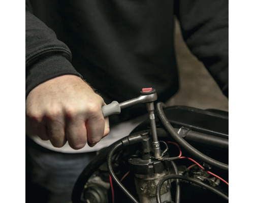 Een persoon gebruikt een ratel met een dopsleutel op een motor.