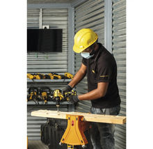 Een man boort met een boormachine een gat in een houten plank die op een werkbank ligt. Op de achtergrond zijn andere boormachines en gereedschappen te zien.
