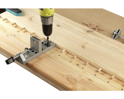 Een boormachine boort gaten in een houten plank met behulp van een deuvelboorapparaat.