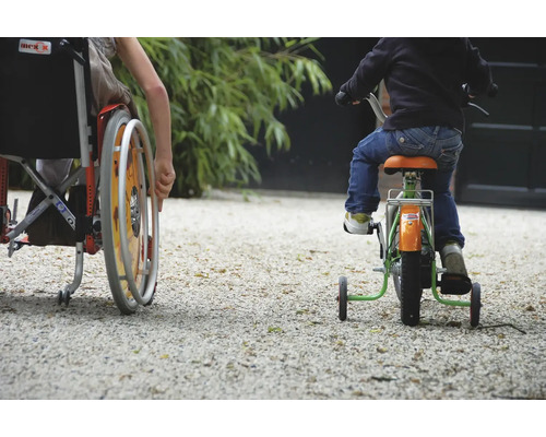 Een kind in een rolstoel en een kind op een driewieler rijden op een grindpad.