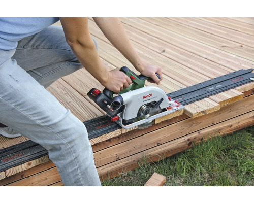 Een persoon zaagt een houten plank met een handcirkelzaag op een houten terras.