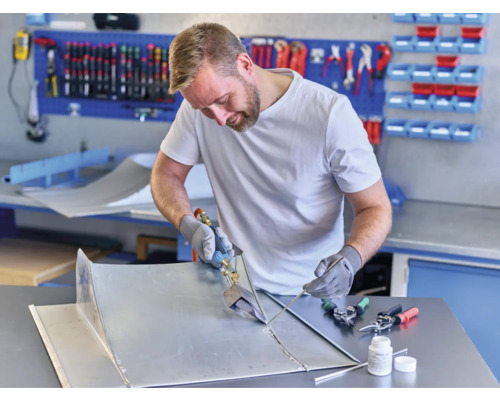 Vakman die metalen onderdelen soldeert in een werkplaats met gereedschap en een werkbank