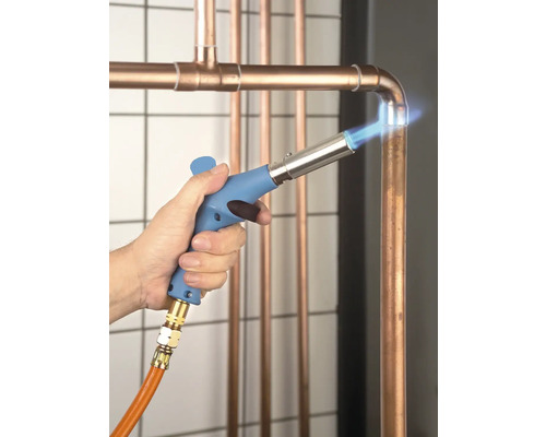 Een vakman soldeert koperen buizen met een soldeerapparaat.