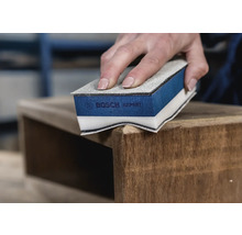 Iemand schuurt een houten meubelstuk met een schuurspons van Bosch Expert