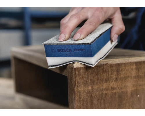 Iemand schuurt een houten meubelstuk met een schuurspons van Bosch Expert