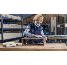 Vrouw schuurt houten plank in werkplaats met schuurblok