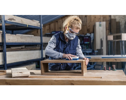 Vrouw schuurt houten plank in werkplaats met schuurblok