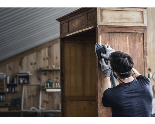 Man schuurt met schuurmachine een houten kast