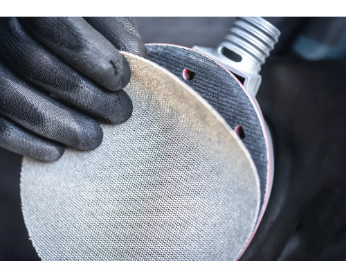 Persoon met beschermende handschoenen houdt schuurschijf vast