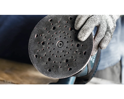 Een handschoen houdt een schuurschijf met gaten vast.