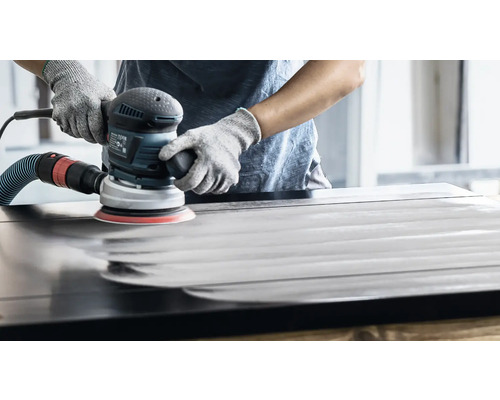 Een persoon schuurt een houten oppervlak met een excentrische schuurmachine.