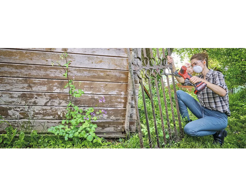 Vrouw werkt met een multifunctioneel gereedschap aan een metalen tuinpoort. Ze draagt een beschermend masker en een veiligheidsbril.