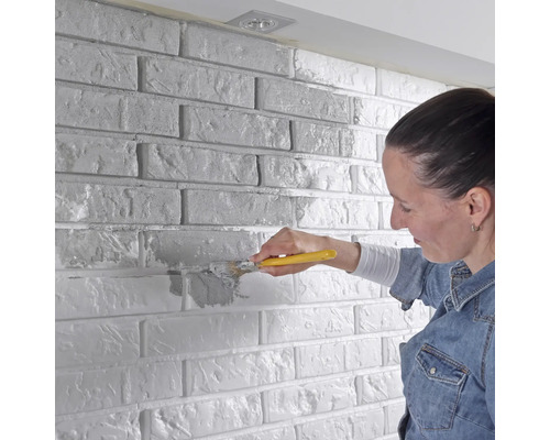 Vrouw schildert bakstenen muur met kwast