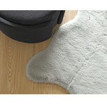 Detail van een grijs tapijt met schapenvachtlook naast een fauteuil op een houten vloer