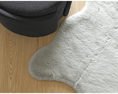 Detail van een grijs tapijt met schapenvachtlook naast een fauteuil op een houten vloer