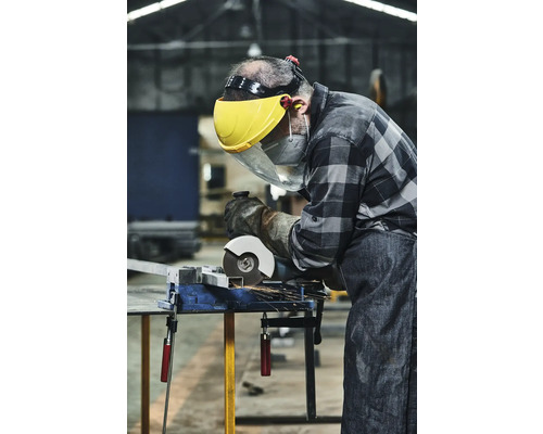 Ambachtsman met veiligheidsvizier en handschoenen snijdt metaal met een slijpmachine op een bankschroef.