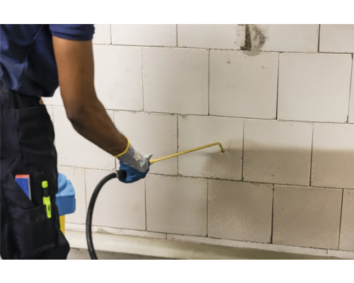 Man spuit vloeistof op een muur van cellenbetonblokken met een spuitapparaat