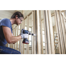 Een man boort met een accuboormachine een gat in een houten frame.