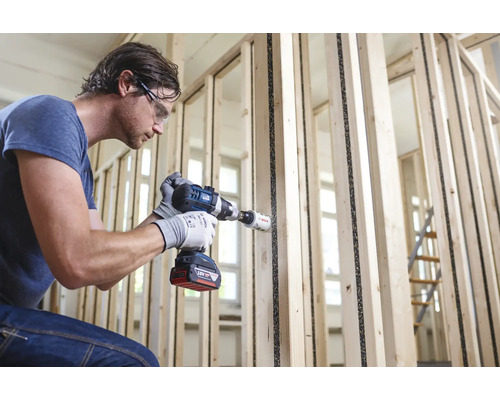 Man boort met een accuboormachine een gat in een houten wand.