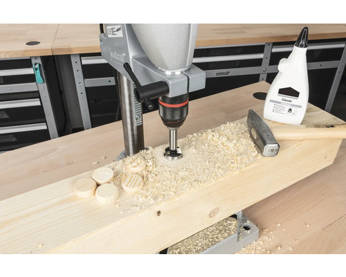 Kolomboormachine boort houten pluggen in een houten plank, met hamer en houtlijm