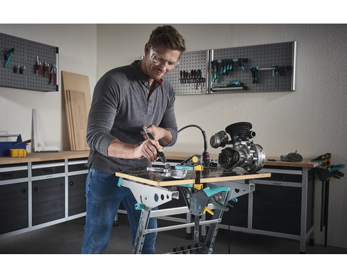 Een man werkt met een werktuig aan een motor op een werkbank in een werkplaats.