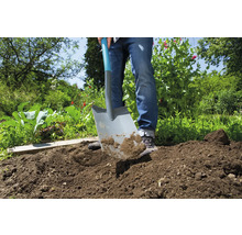 Iemand graaft met een spade in de tuin de grond om.