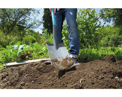 Iemand graaft met een spade in de tuin de grond om.