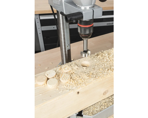 Kolomboormachine tijdens het boren van een gat in een houten plank met houtsnippers en houten schijven