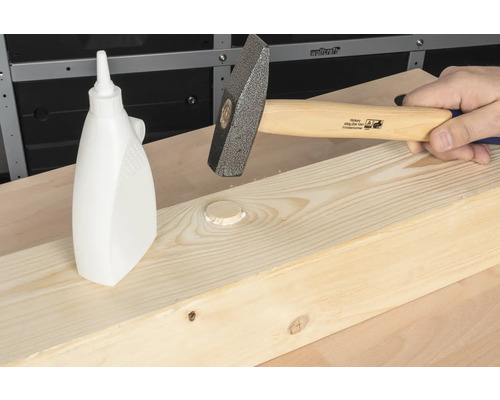 Hamer slaat houten deuvel in een houten plank naast een fles houtlijm