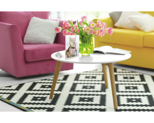 Woonkamer met roze fauteuil, gele bank, ronde tafel en vloerkleed met geometrisch patroon