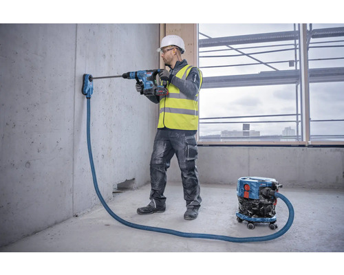 Ambachtsman boort met een boorhamer een gat in een betonnen muur met stofafzuiging
