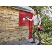 Vrouw schildert houten muur rood met verfspuitsysteem