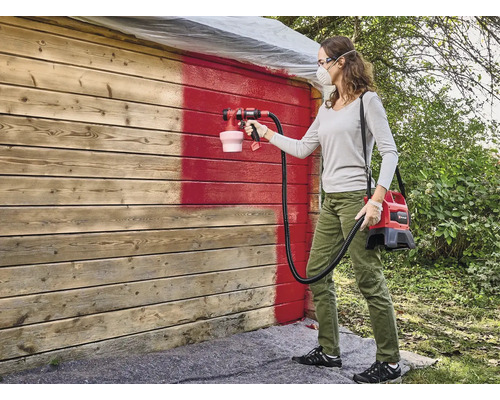 Vrouw schildert houten muur rood met verfspuitsysteem
