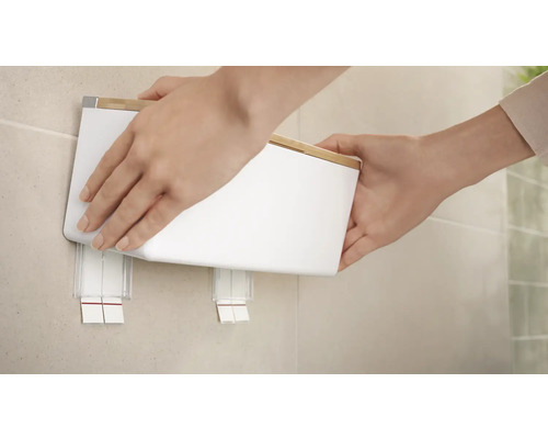 Een persoon bevestigt een witte papieren handdoekdispenser met bamboedeksel aan de muur.